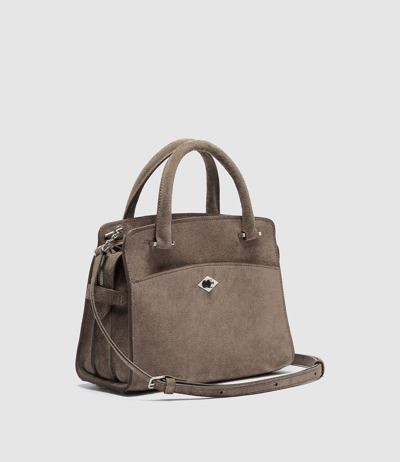 A taupe brown suede handbag with dual top handles, a detachable shoulder strap, and a small diamond-shaped silver logo clasp on the front, placed on an angle.